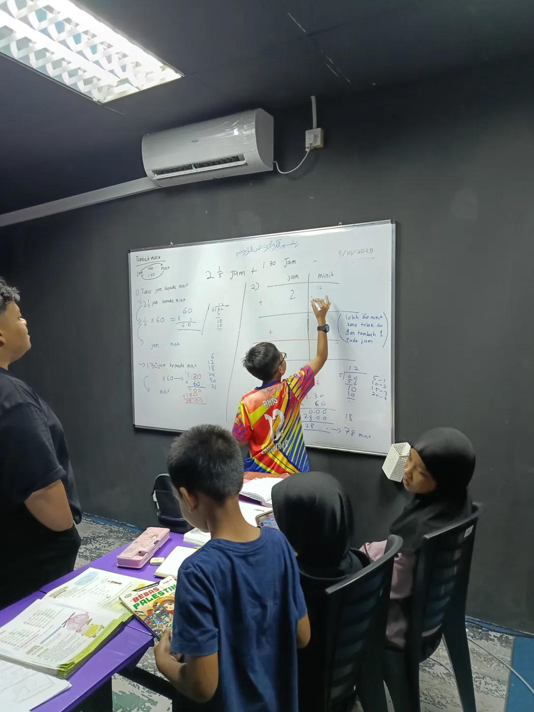 Pelajar menulis jawapan di papan putih sambil diperhatikan rakan